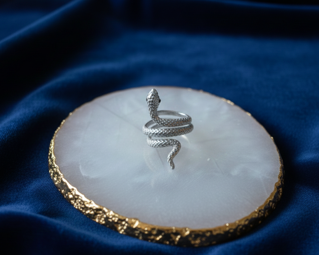 Silver snake ring on a white stone with gold edge against a blue fabric background