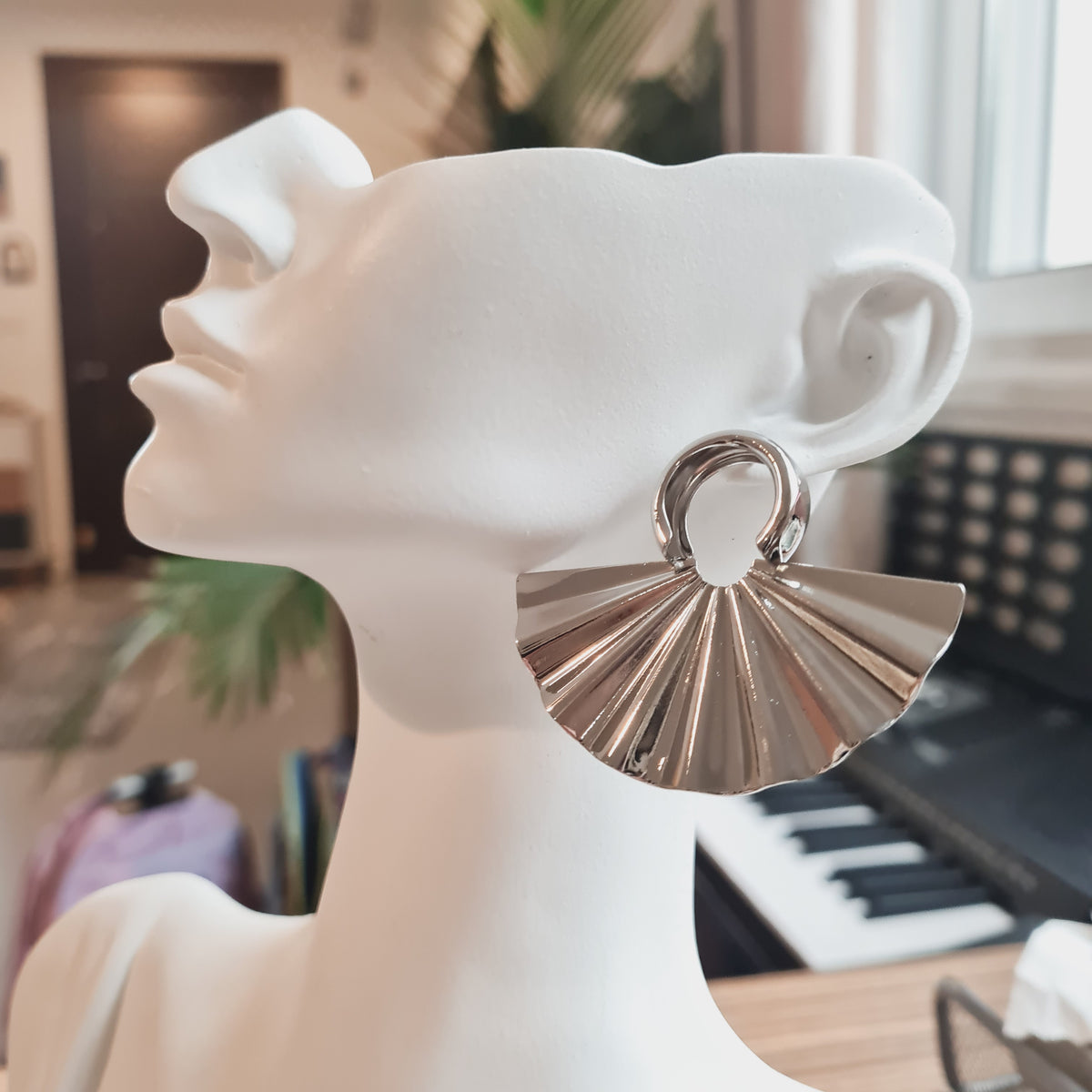 Silver-tone pleated fan-shaped earring with an oval hoop on a white display bust
