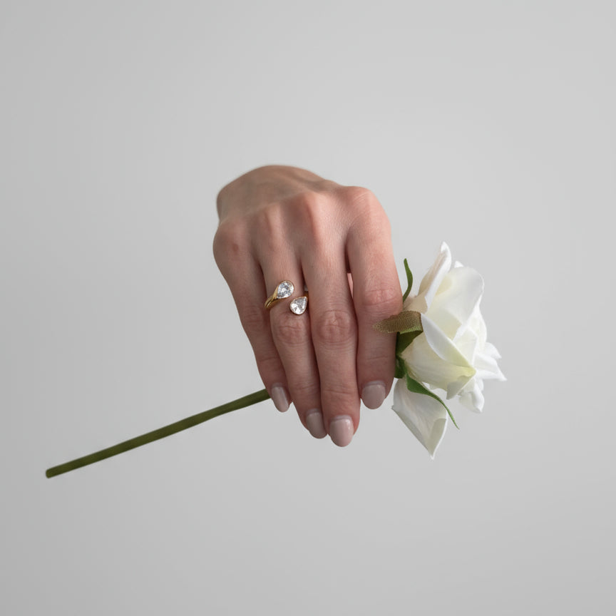 Embrace understated elegance with the Serenity Dual Crystal Ring — a modern open-band design that captures light and grace in every movement.

Featuring two shimmering crystals — a teardrop and a round cut — set on a polished gold band, this piece embodies effortless sophistication and balance.