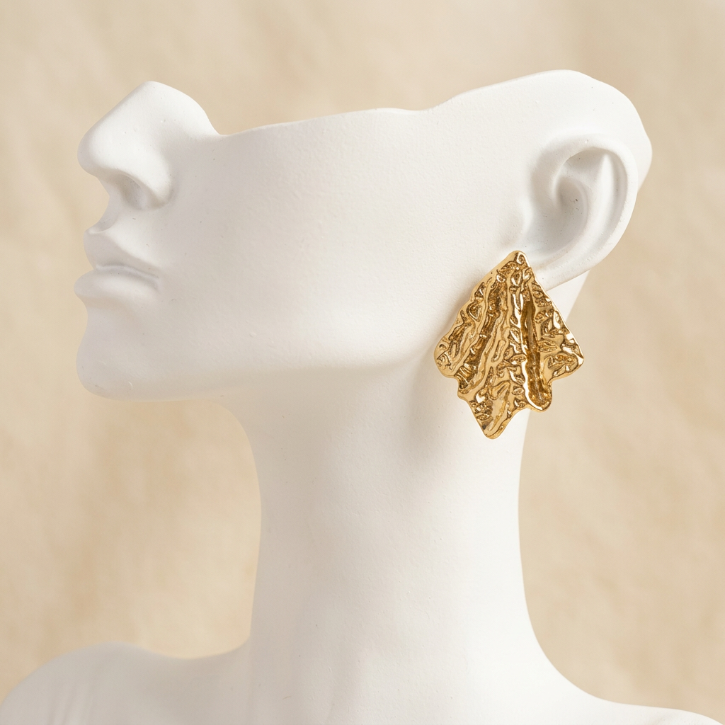 Gold-tone textured sculpted leaf earring on a white display bust