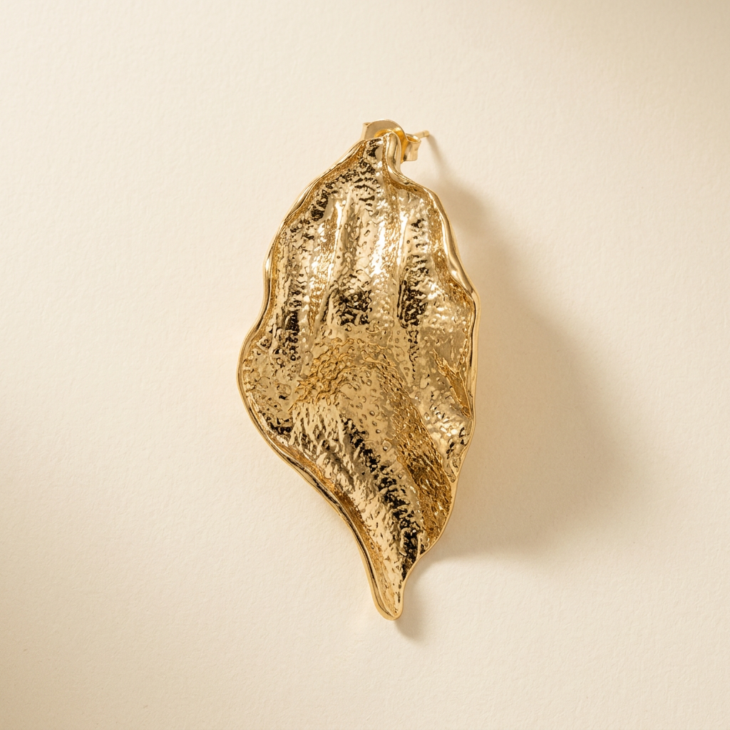 Gold-tone textured sculptural petal earring on an ivory background