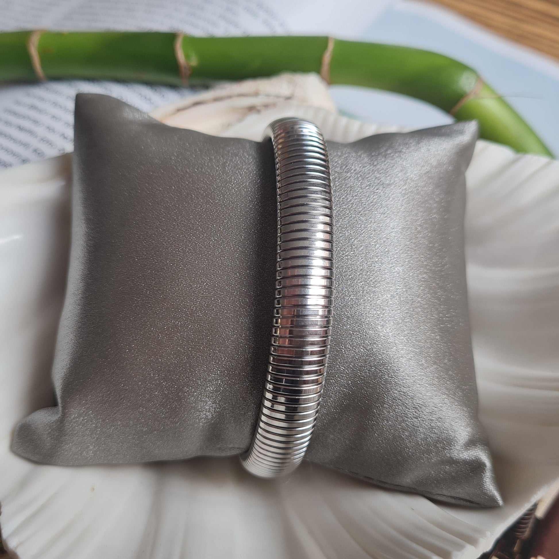 An elastic bracelet made of stainless steel, displayed on a cushion, with a magazine in the background.